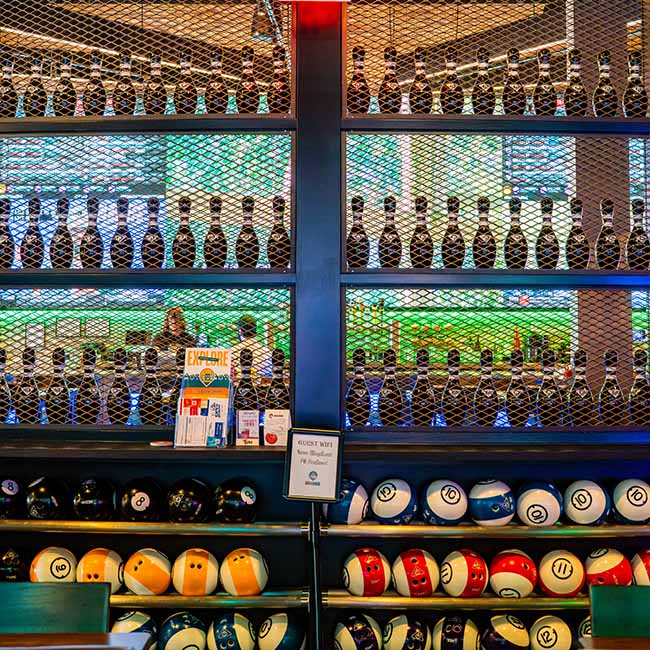 Bowling balls and pins are displayed behind a mesh wall at a colorful private events bowling alley.