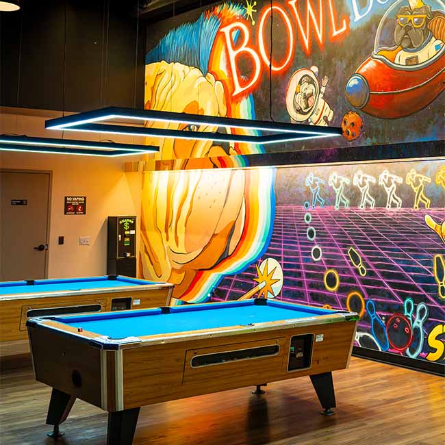 Two pool tables in a North Liberty Iowa game room with arcade vibes and a space-themed mural.